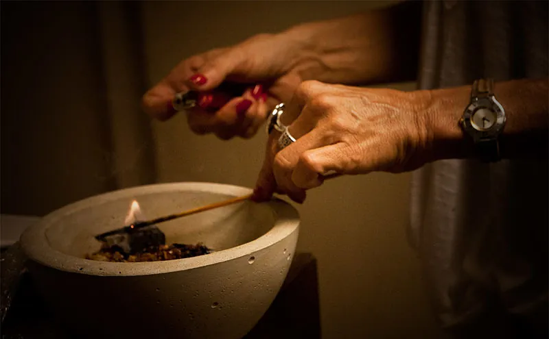 Magia: mano encendiendo incienso en un cuenco a la luz de una vela